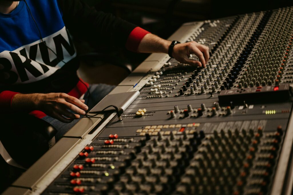 pexels-photo-4988131-4988131 Sound engineer adjusting audio levels on a mixing console in a modern recording studio.